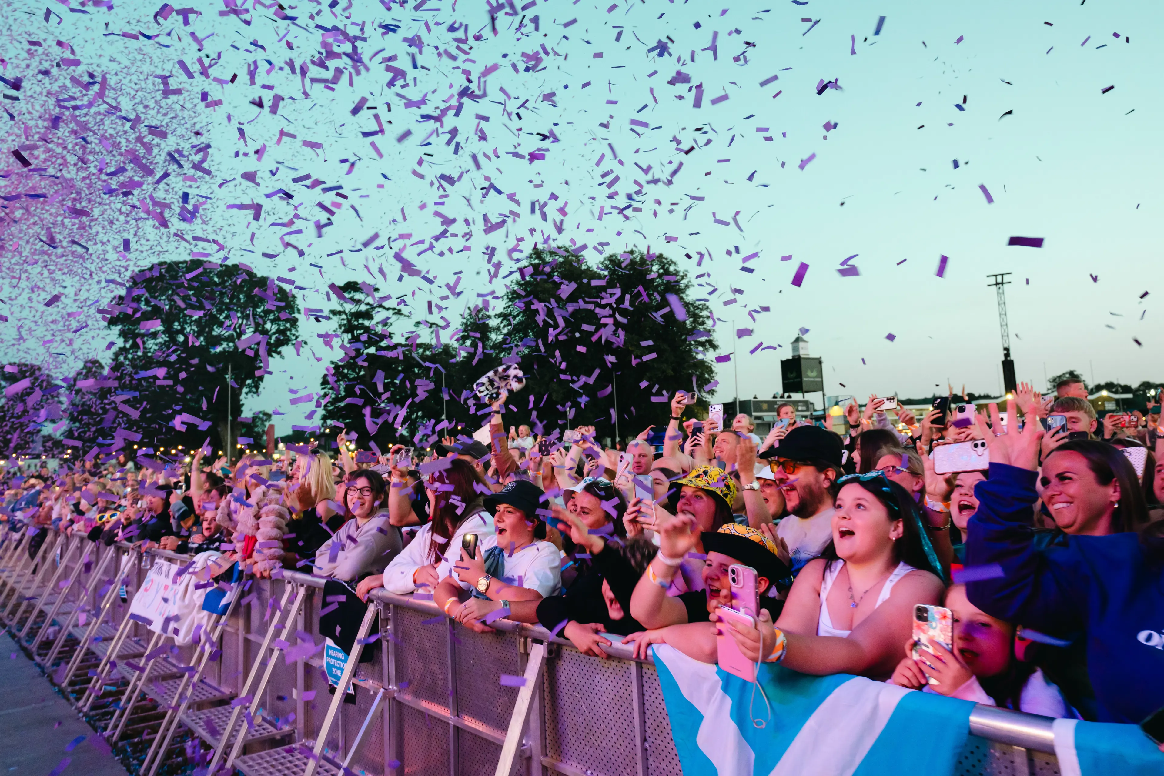 Front-row festival crowd cheers and films as purple confetti rains down.