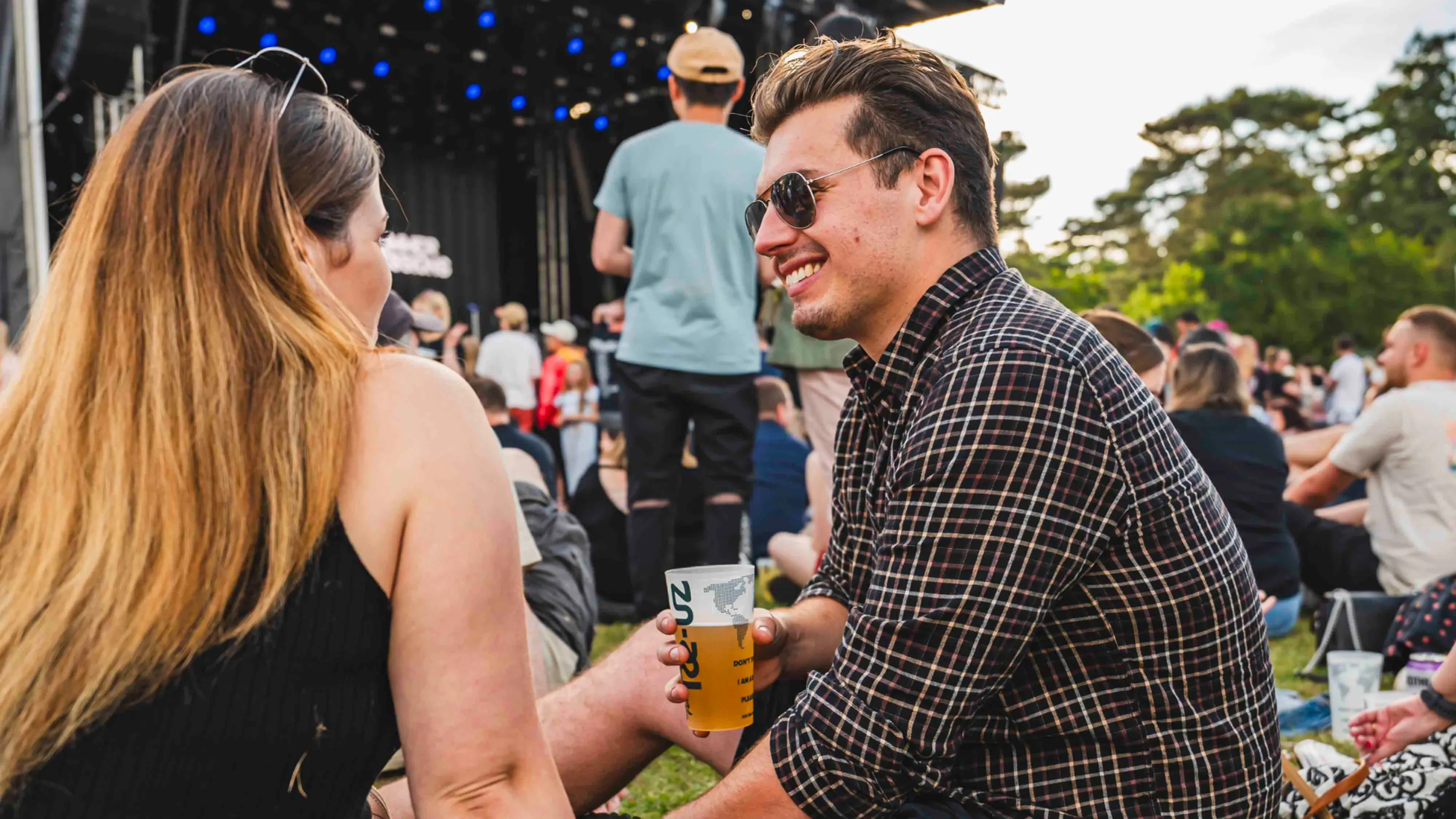 Two fans in the VIP section at TK Maxx presents Bedford Summer Sessions smiling, enjoying a drink by the main stage. 