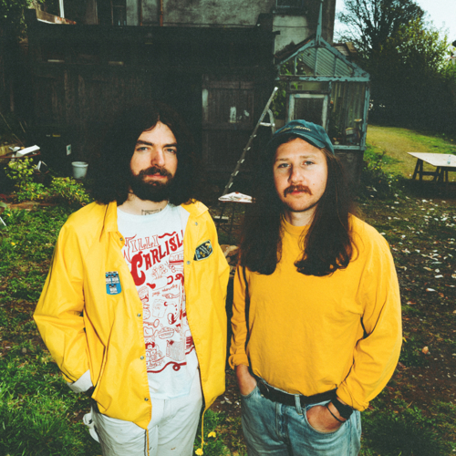 artists DUG wearing matching yellow cardigans standing outside a home