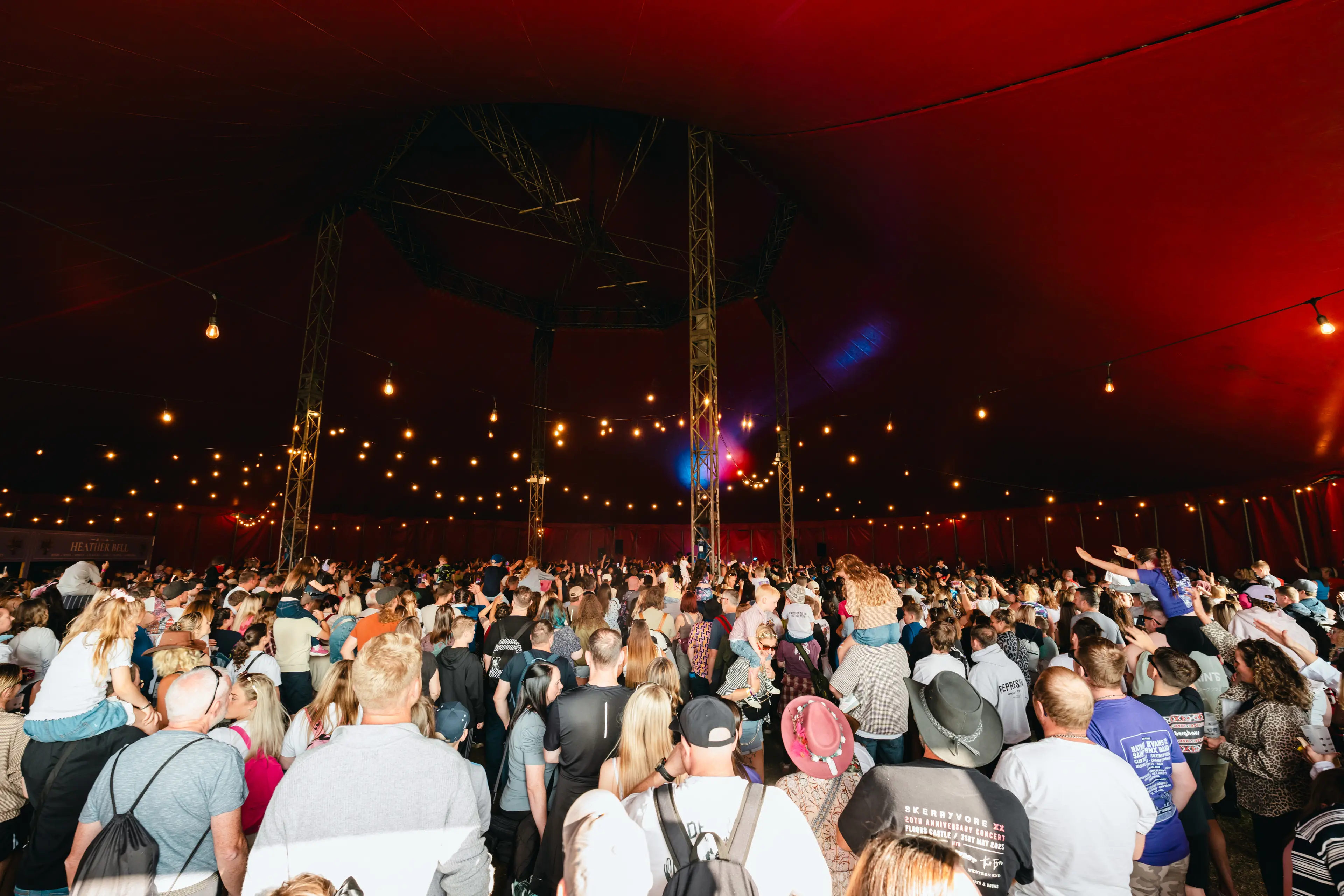 Packed audience inside a large red festival tent lit by strings of warm bulbs.