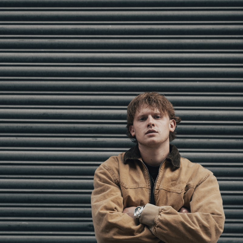 artist Bec O'Malley standing in front of a garage with arms crossed