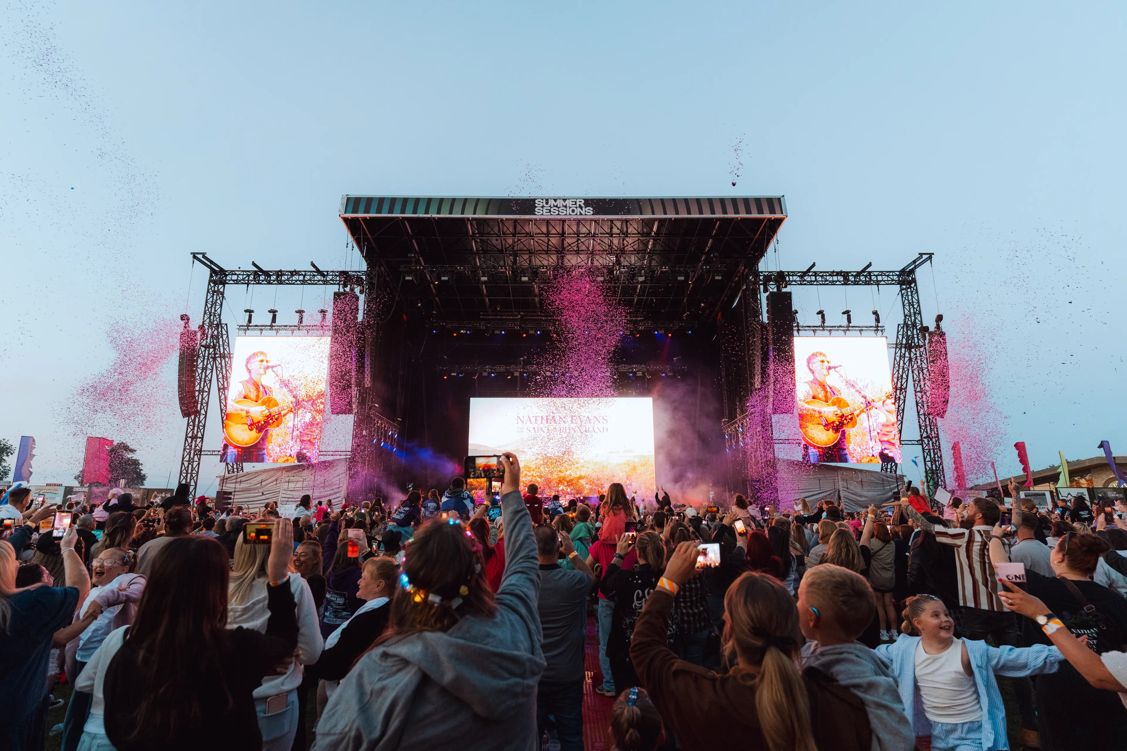 Crowd films Nathan Evans performing as pink confetti erupts around the main stage.