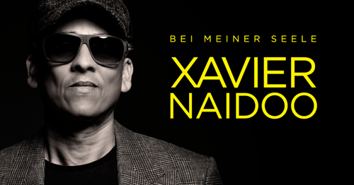 Man sieht Xavier Naidoo in mit seinen Markenzeichen, der Sonnenbrille sowie der sogenannten Schiebermütze. Daneben ist sein Name in gelben Buchstaben geschrieben.