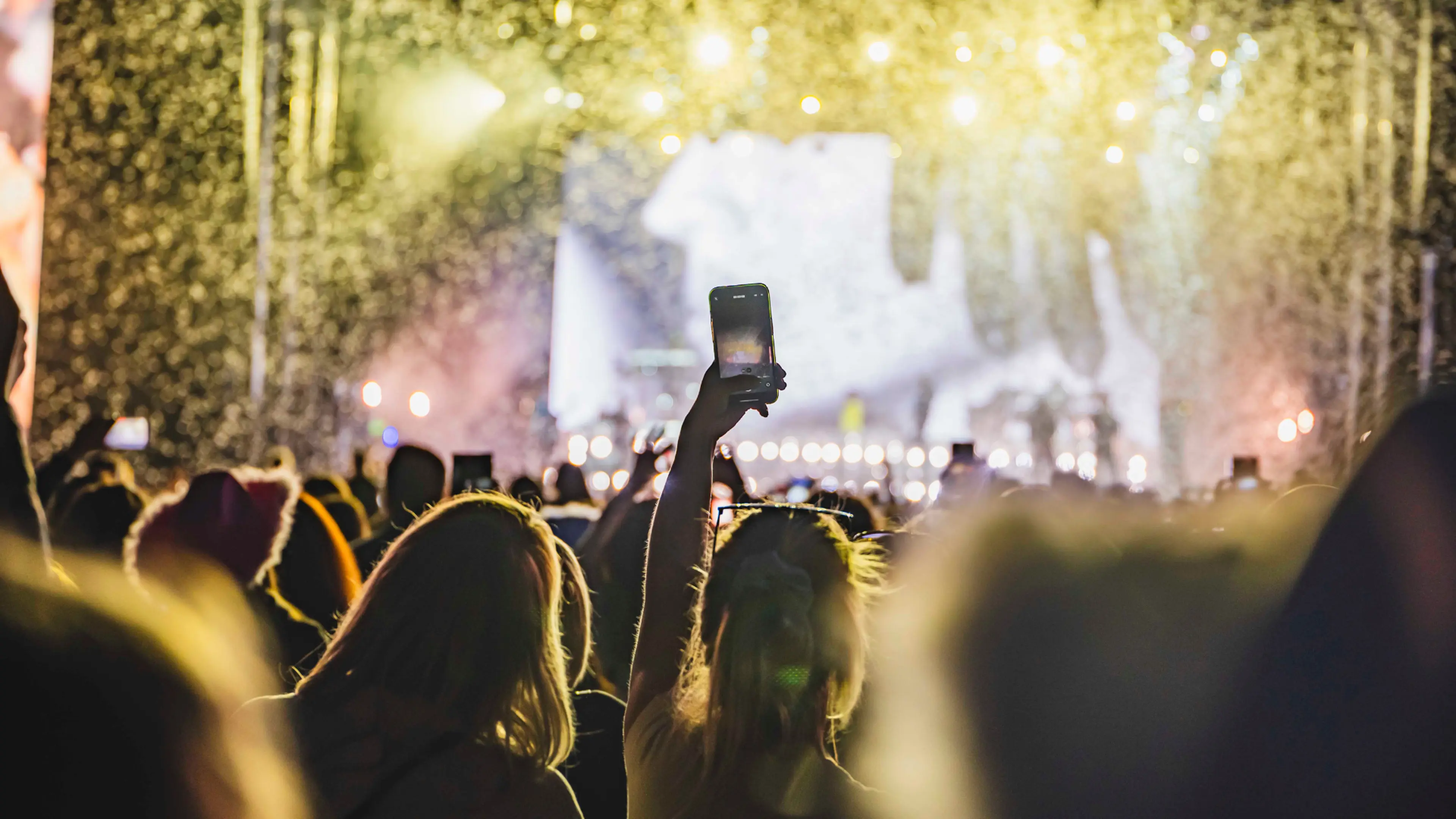 Crowd shot with a fan holding up their phone filming the stage. 