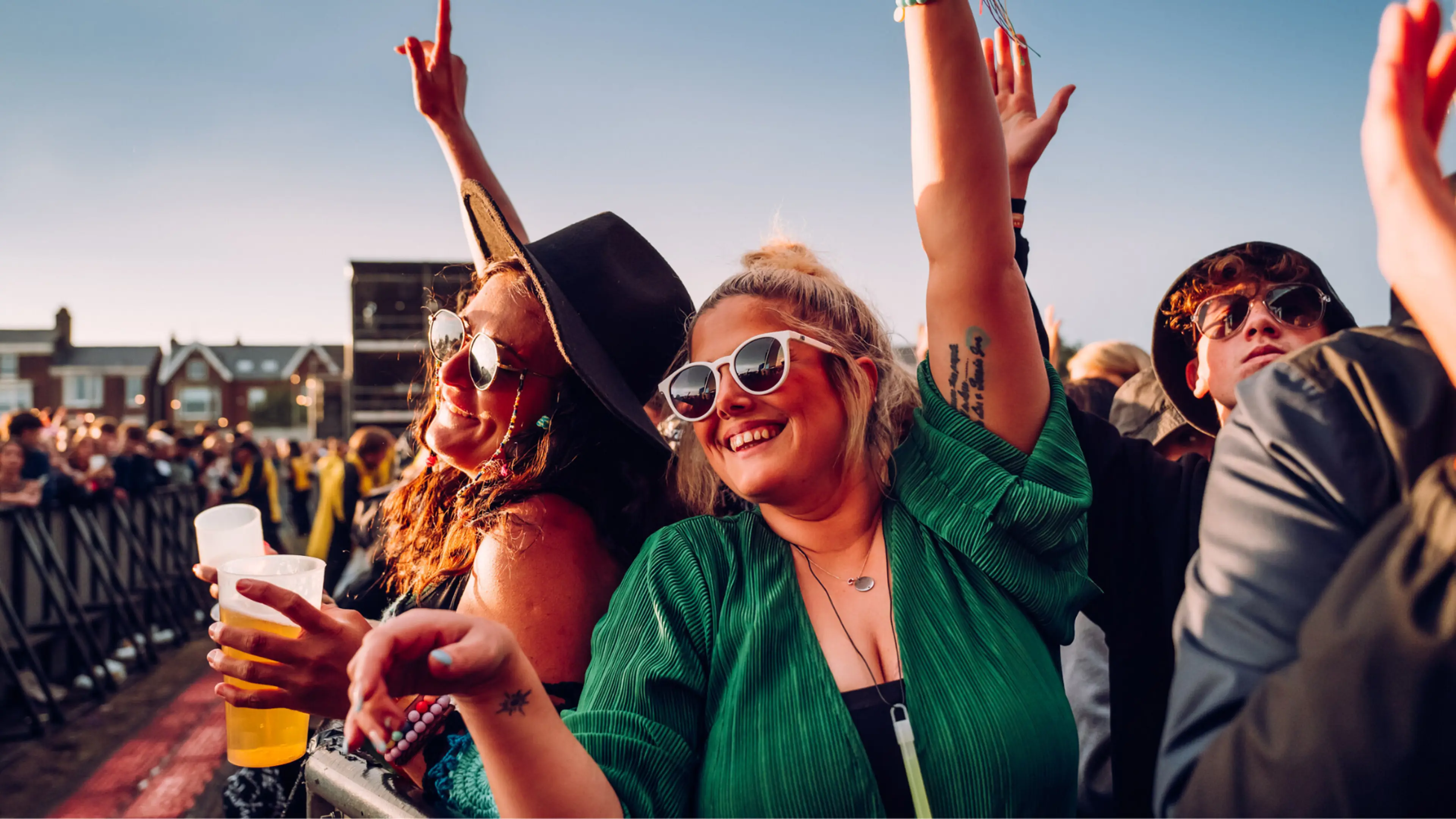 Fans in the crowd with their hands raised in the air smiling with a drink enjoying the show. 